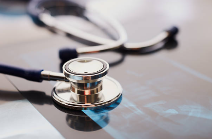 Medical stethoscope resting on a reflective surface with blue-tinged medical images in the background, suggesting healthcare examination.