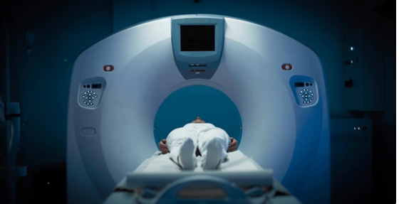 Patient lies on an MRI table about to enter a large circular MRI scanner in a dimly lit room, hospital setting.