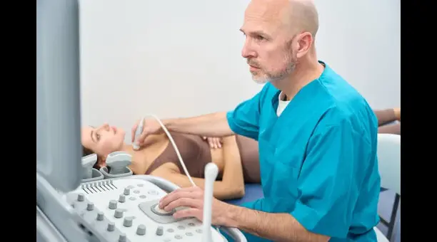 EBUS-endobronchial-ultrasound - drmanumadan.com Medical professional in blue scrubs performs an abdominal ultrasound on a patient lying on an exam table, using a handheld transducer.